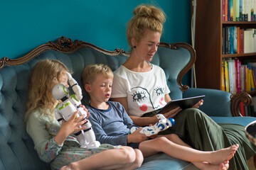 Woman using digital tablet while kids with robots sitting on sofa in living room at home