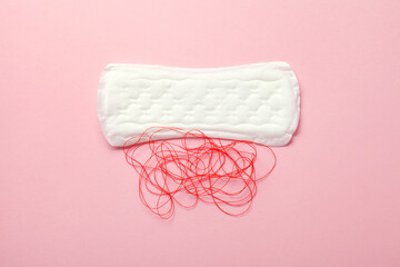 Menstruation pad with red thread as blood over pink background, women critical days, gynecological concept, menstruation cycle