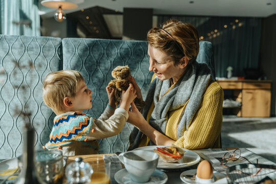 Mother and son playing with toy animal while sitting at table in hotel