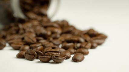 roasted coffee beans Get ready for the grind being poured out of a glass bottle laid on a white background To make fresh coffee or go into an espresso machine or Moka Pot