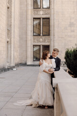 Photo of young couple bride and groom in wedding dresses on background of concrete building in city. Happy wedding day together.