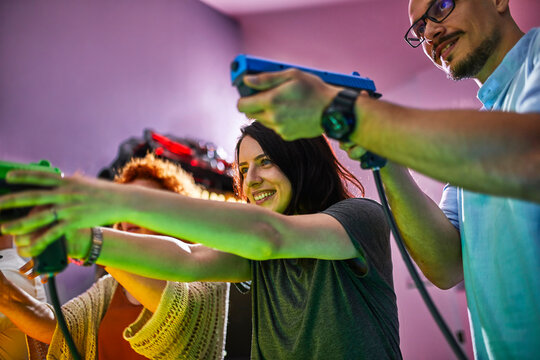 Happy friends playing and shooting with pistols in an amusement arcade