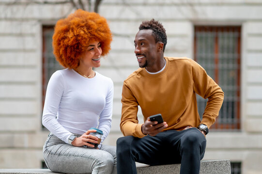 Smiling woman with disposable cup talking with man while sitting on bench