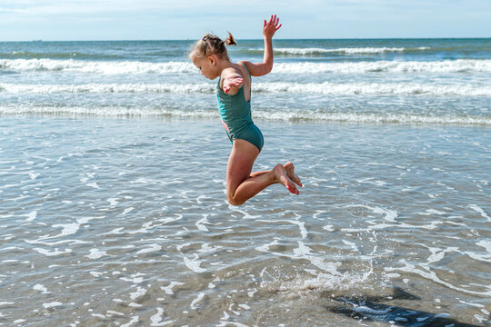 Girl gymnast jumping over sea at beach on sunny day - Powered by Adobe