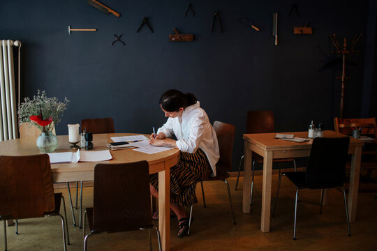 Female owner analyzing financial bills on table while sitting in coffee shop