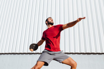 Young man practicing disc throw while standing against wall