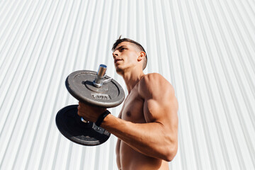 Young athlete lifting dumbbell while standing against wall