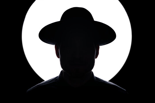 In silhouette of man wearing hat standing against illuminated lighting equipment