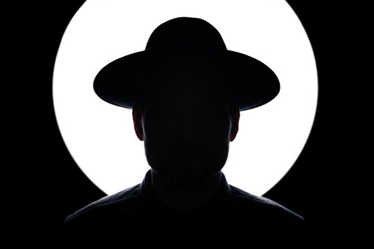 In Silhouette Of Man Wearing Hat Standing Against Illuminated Lighting Equipment