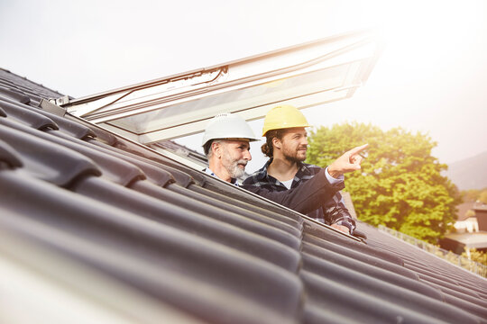 Two men wearing hard hats looking out of roof window