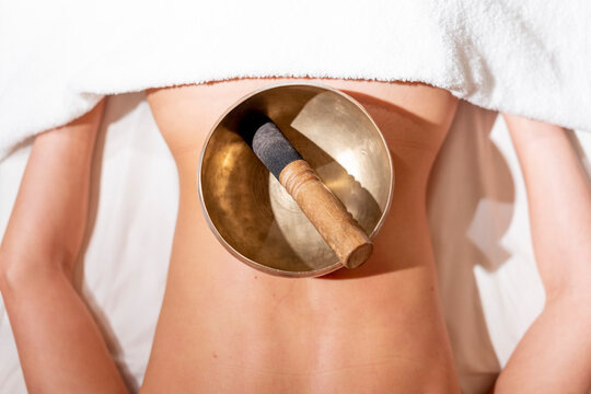 Mallet in rin gong on female customer's back lying on massage table at health spa