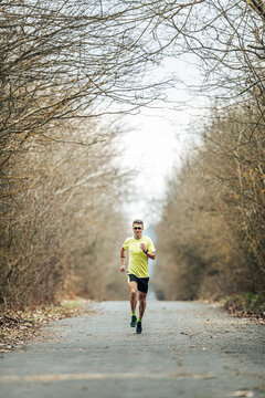 Young male athlete running on country road amidst bare trees