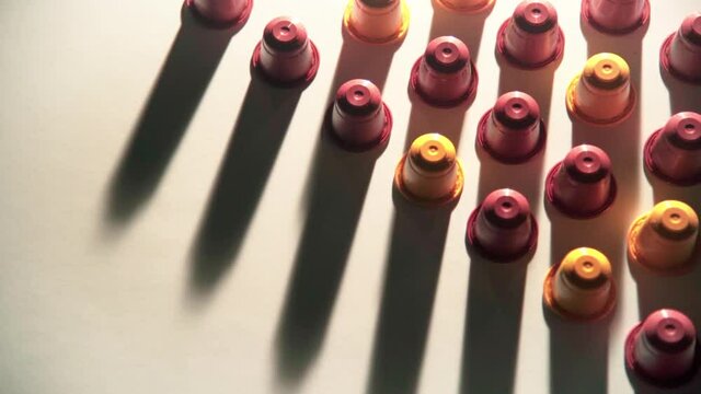 Red and yellow coffee capsules line up on white table with changing shade 50fps