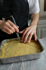 Making sweet pastries at home. Baklava prepared for baking in a baking sheet. The hands of the cook cut the dough into pieces with a knife..