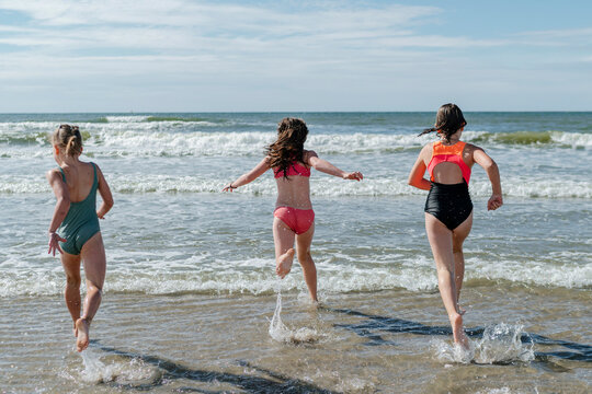 Friends running in water at beach on sunny day