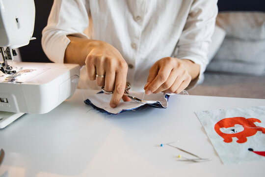 Woman cutting thread with scissors while making homemade face mask