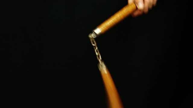 Man's hand holding a nunchaku in his hand twirling it. White weapon concept.