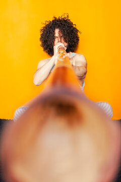 Crazy man with curly hair playing didgeridoo while sitting against yellow background