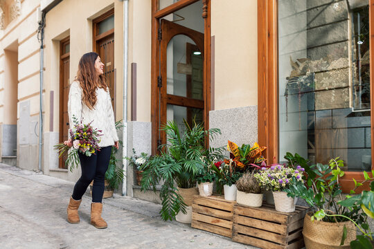 Woman with bouquet standing and looking at flower shop