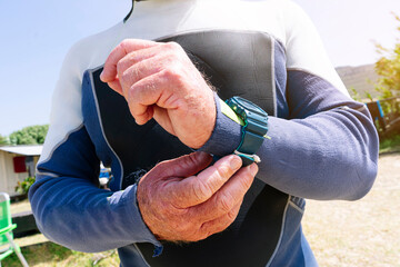 Close-up of senior man wearing wetsuit adjusting wristwatch at beach during sunny day