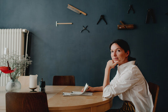 Female owner with menu sitting at table against wall in restaurant