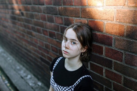 Serious teenage girl with blue eyes leaning on brick wall in city