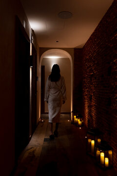 Young female customer wearing bathrobe walking in dark corridor at health spa