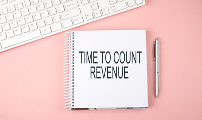 Pink office desk with keyboard and notebook with text TIME TO COUNT REVENUE