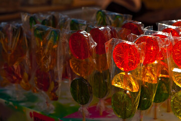Many colorful lollipops on a stick. Sweets are sold at the city fair. Contrasting dramatic light as an artistic effect.