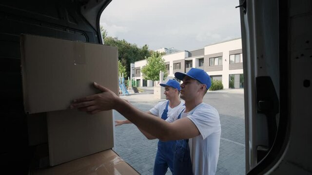 Two young workers of removal company are loading boxes and furniture into a minibus