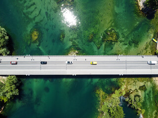 Aerial drone view of bridge above beautiful green river. Cars and pedestrians moving on bridge, view from above. Transportation. Modern concrete bridge over the lake.