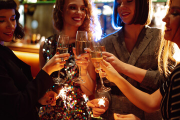 Glowing sparkles in hands. Young  friends celebrate new year and holding bengal lights and glasses...