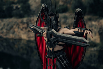 Daemon of death with wings stands with black sword among water and rocks.