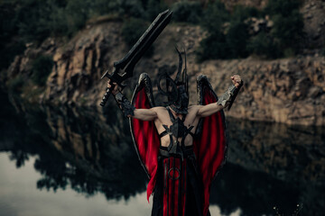 Daemon of death with wings stands with raised black sword among water and rocks.