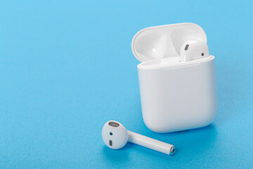 Modern wireless bluetooth headphones with charging case on a blue background. The concept of modern...