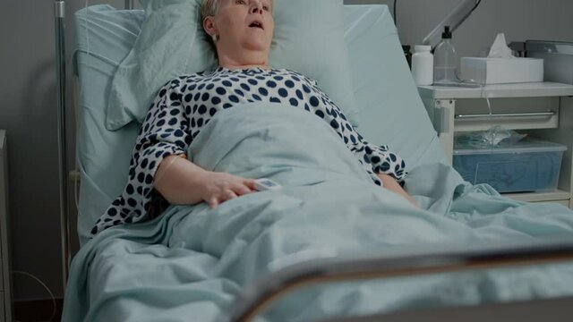 Doctor and nurse using oxygen tube for hyperventilating woman in bed. Medical specialists with tool and heart rate monitor for reanimation and respiratory problem of senior patient.