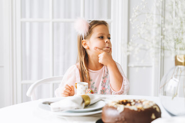 Obraz na płótnie Canvas Funny cute little girl with long hair in light pink dress with chocolate cake in hands on festive table in bright living room at home. Christmas time, birthday girl