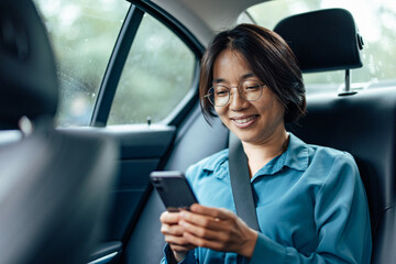 Businesswoman using smart phone on a backseat of a car.