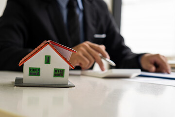 Real estate agents offer contracts for home insurance and investment loans. A house model and a customer discuss a home contract, insurance, or real estate loan at their office desk.