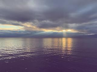 Fototapeta na wymiar Fantastic lake surface with reflection of the sunlight, sunrays through the dark cloud