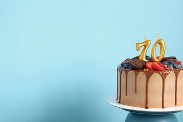 Chocolate birthday cake with berries, cookies and number seventy golden candles on blue wall...