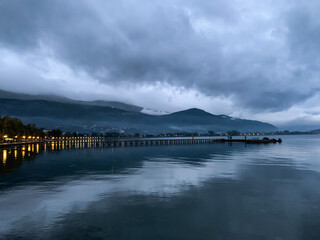 Long pier at the lake, twilight, dark blue and gray sky and lake, mountains background