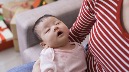 female cradling an adorable baby girl in her arms who is in a deep sleep and breathing with mouth during daytime at home.