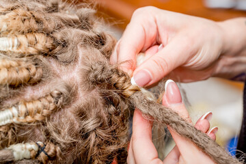 Dreadlocks African braids are weaved by a master hairdresser in the salon, head and hair close-up...