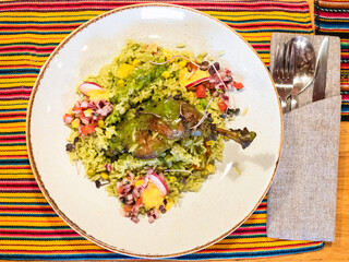 top view of Arroz con Pato - Peruvian dish from duck leg stewed in beer with cilantro, with green rice on plate on table in local restaurant