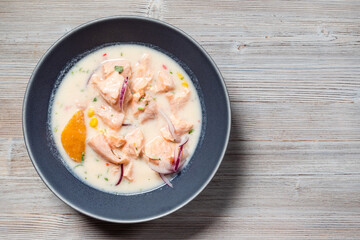 top view of peruvian Salmon ceviche in Leche de Tigre sauce with sweet potatoes and corn in bowl on gray wooden table with copyspace