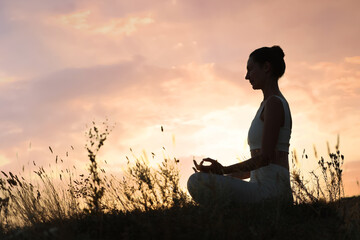 Mature woman meditating outdoors at sunset. Space for text