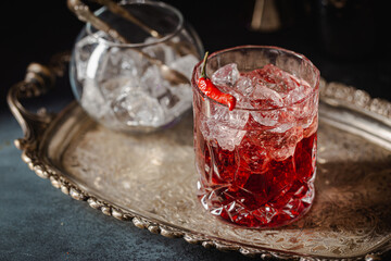 Red alcoholic cocktail with ice and red chili garnish