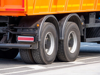 Dump truck wheels with all-season tires on an asphalt road. A close-up of the rear axles of a truck. Construction machinery in the city - obrazy, fototapety, plakaty