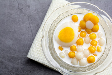 Pumpkin (white and yellow) rice dumpling in coconut milk (Bua Loy) in transparency bowl on wooden table. Delicious Thai dessert.